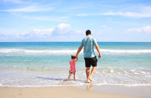 father and daughter at the beach facing ocean